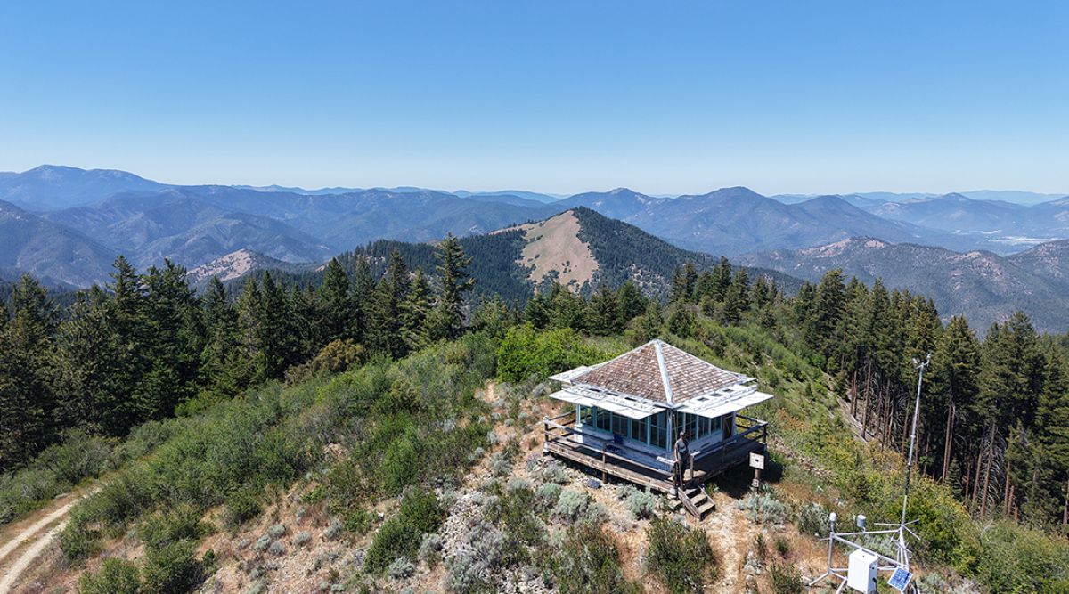 Acorn Woman Lookout with woman standing on the porch - expansive view of the Siskiyou Mountains in the late spring.  