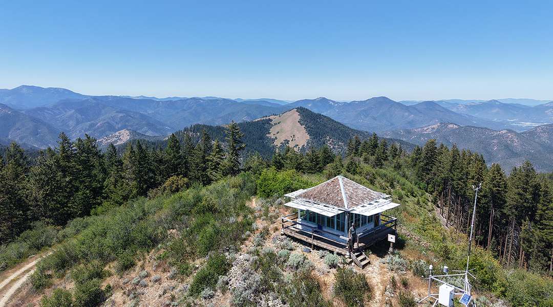 Acorn Woman Lookout with woman standing on the porch - expansive view of the Siskiyou Mountains in the late spring.  
